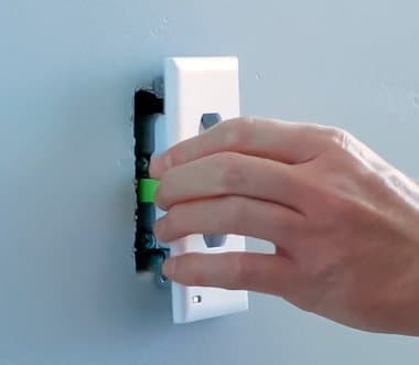Hand fitting a GuideLight over an outlet, showing the metal prongs that slide around the side screws