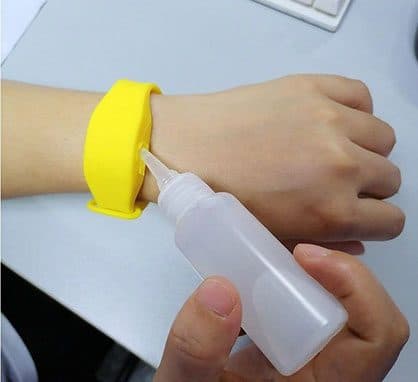 Yellow silicone sanitizer wristband on a wrist being refilled from a small squeeze bottle with a long nozzle