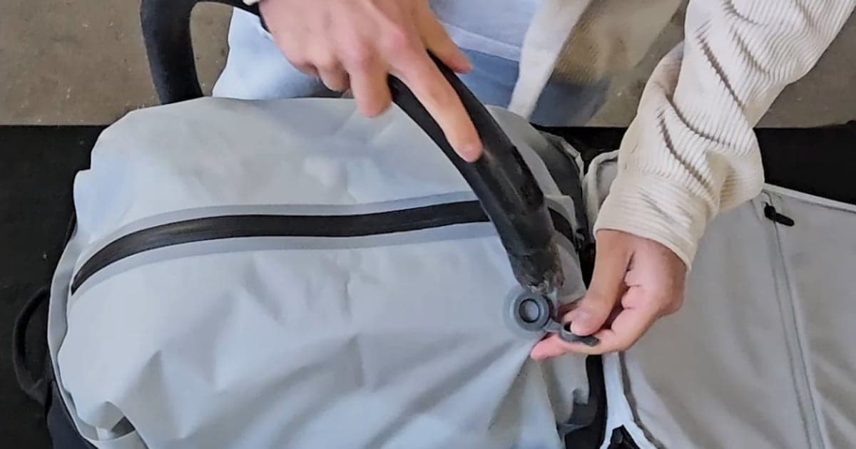 A hand opening the cap on the valve of a grey Aerless vacuum bag, with a household vacuum cleaner hose ready beside it