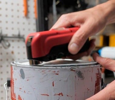 Hand tapping down a paint can lid with the hammering face of a red Kelvin 17