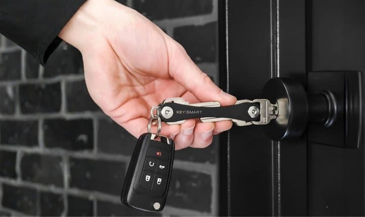 Hand unlocking a front door with a KeySmart key while a car fob hangs from its loop