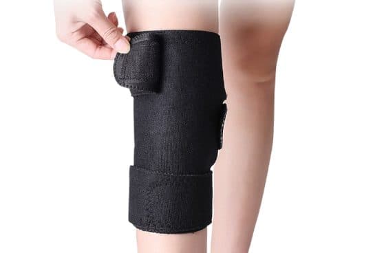 Hand fastening the top strap of a black KneeWrap Pro neoprene-style knee wrap with a lower strap already closed below the kneecap