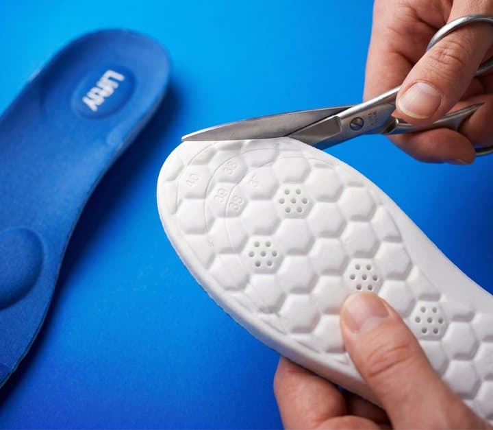Scissors trimming the toe end of a Liftly insole along the printed size lines