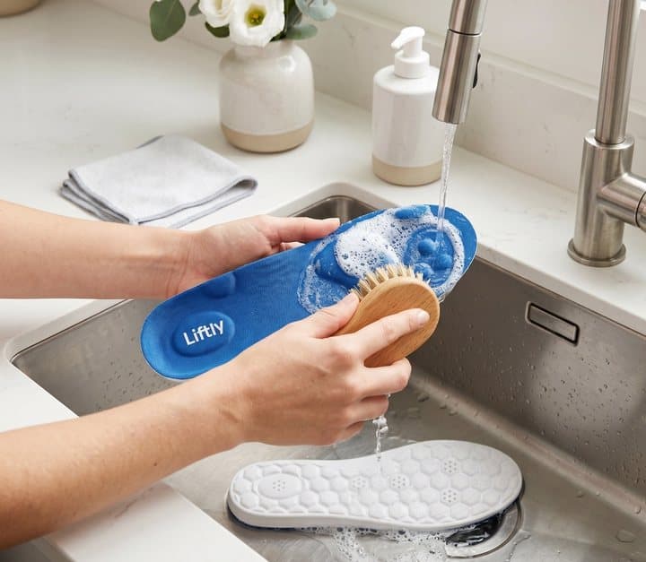 Hands scrubbing a Liftly insole with a brush under a kitchen tap