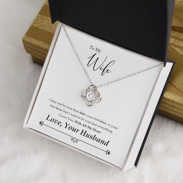 Love Knot Necklace in a black and white box on a To My Wife card signed Love, Your Husband, resting on white fur beside a gold-striped gift box