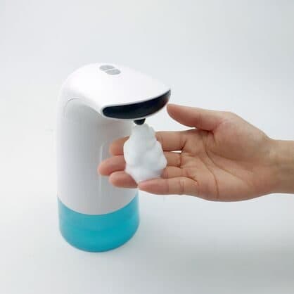 White touchless foam soap dispenser with a blue base dispensing foam onto a hand