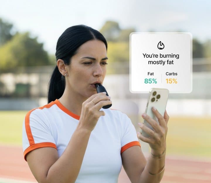 Woman in sportswear breathing into Lumen with a phone showing she is burning mostly fat