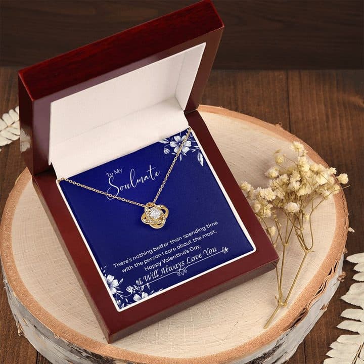 Gold-tone Luxury Love Knot in an open mahogany-style box on a wooden slice beside dried flowers