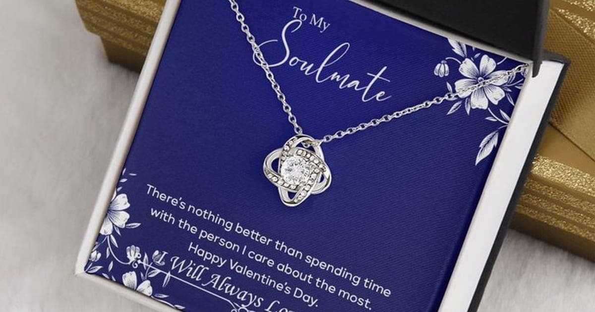 Silver-tone Luxury Love Knot pendant with a clear stone on a navy To My Soulmate card with white flowers, in an open black box beside a gold gift box