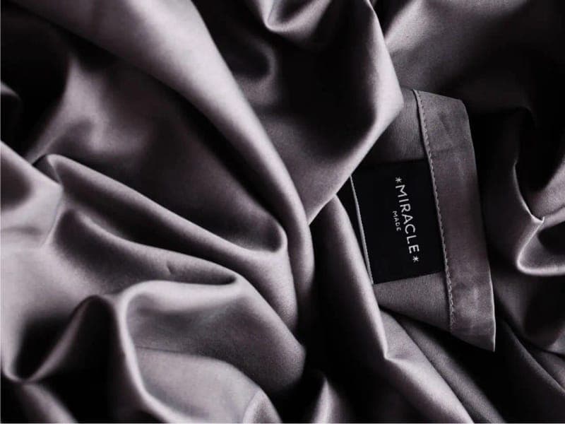 Close-up of rumpled grey Miracle Made cotton sateen showing the sheen of the weave and the Miracle label