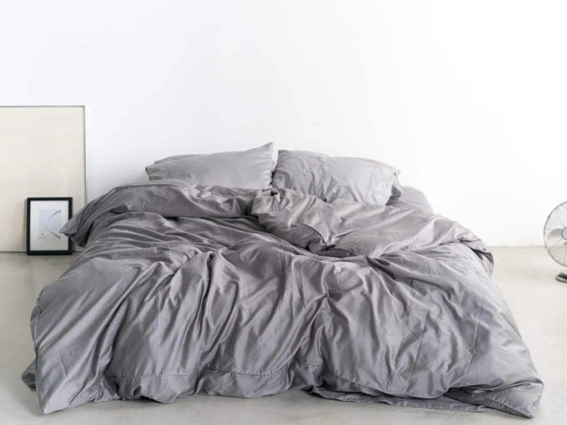 Bed made up with grey Miracle Made sateen sheets, pillowcases and duvet cover in a bright room