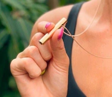 Fingers holding a small gold Moksha Beam pendant on its chain to show its size