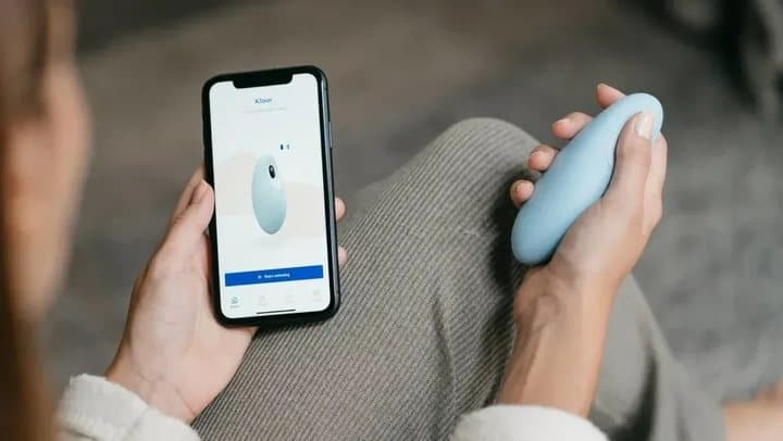 Person holding a pale blue Moonbird while looking at the Moonbird app on a phone