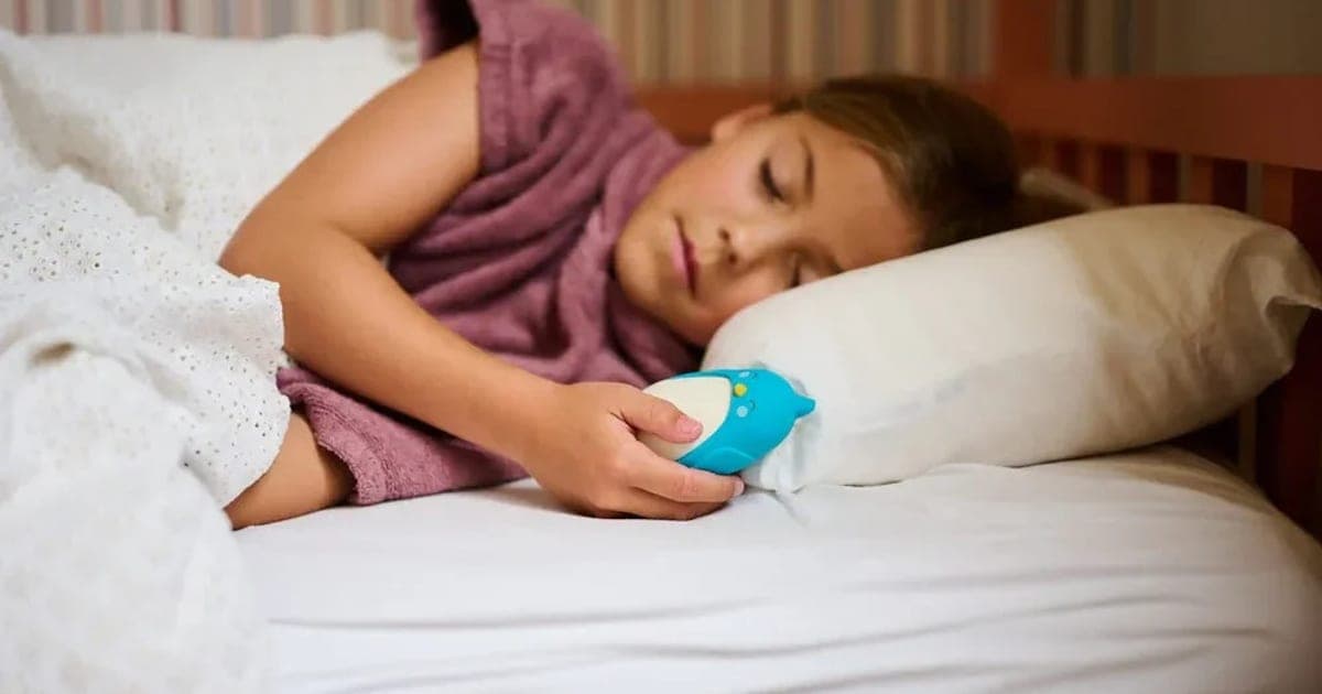 Girl lying in bed with her eyes closed holding a blue Moonbuddy bird breathing device