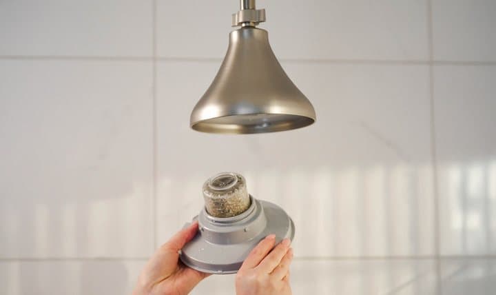 Hand holding the NUUD filter cartridge below the shower head