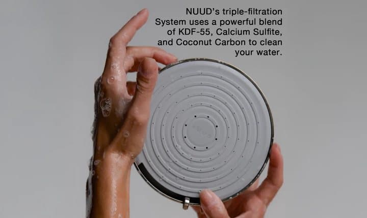 Hand holding the NUUD shower head face with text describing KDF-55, calcium sulfite and coconut carbon filtration