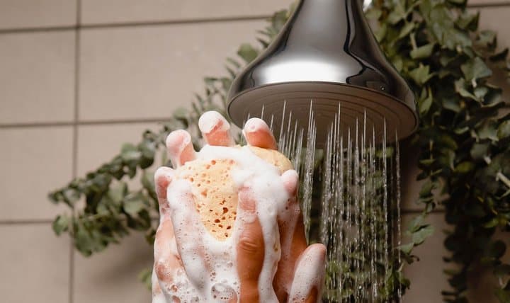 Hands lathering soap under water from a chrome NUUD shower head