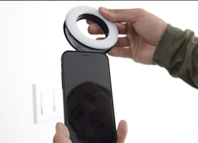 Hand clipping an OlumiRing ring light onto the top of a smartphone
