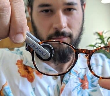 Man cleaning both sides of an eyeglass lens with Peeps carbon pad tongs