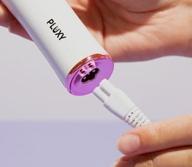 Close-up of the Pluxy epilator head with its tweezer discs, plugged into a charging cable