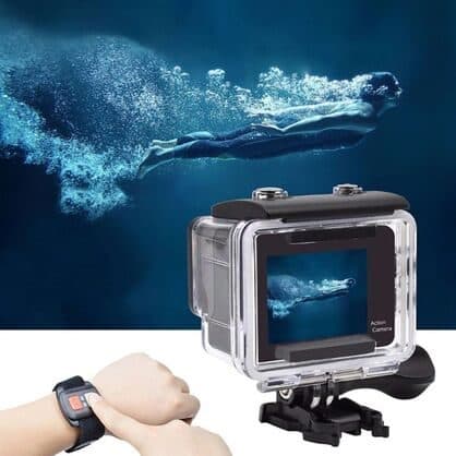 Swimmer underwater above an action camera in a clear waterproof case, with a hand pressing a red button on a wrist remote