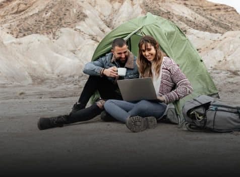Couple sitting outside a tent using a laptop in a rocky landscape