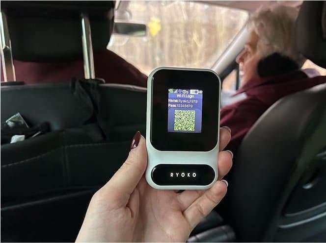 Hand holding a Ryoko PRO hotspot in the back seat of a car