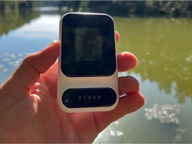 Hand holding a Ryoko PRO hotspot beside a lake
