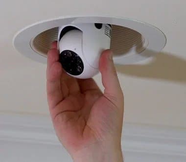 Hand screwing a white Sight Bulb camera into a recessed ceiling light socket
