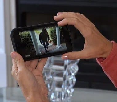 Hands holding a phone showing a live Sight Bulb view of a person walking up to a front door