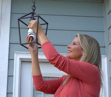 Woman fitting a Sight Bulb camera into a black lantern-style porch light outside a house