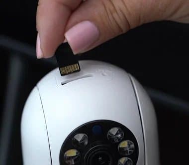 Close-up of a hand inserting a memory card into a slot on the white Sight Bulb camera body