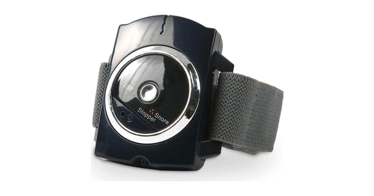 The Sleep Connection anti-snore wristband, a black round device with a silver ring and grey fabric strap, printed with the words Snore Stopper
