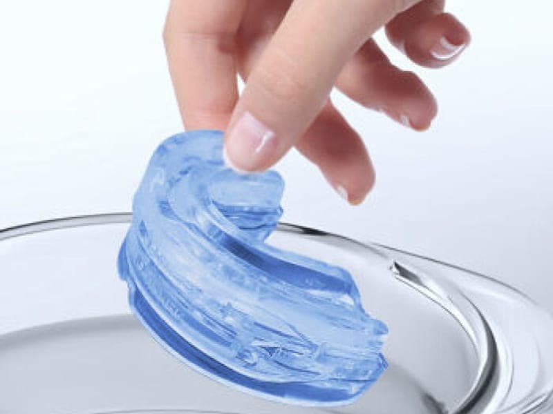 Hand lifting the SleepZee mouthpiece out of a bowl of hot water after softening it for moulding