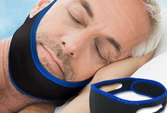 Grey-haired man asleep on a pillow wearing the black Snore Strap with blue edging under his chin and over his head