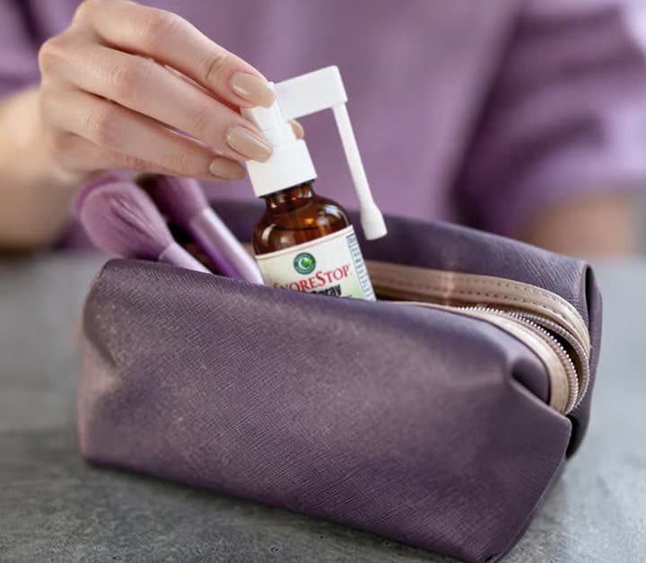 Hand putting a SnoreStop bottle into a purple toiletry bag