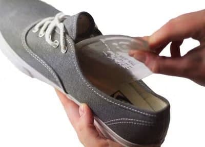 Hand placing a clear Soul Insole gel insert into a grey canvas sneaker
