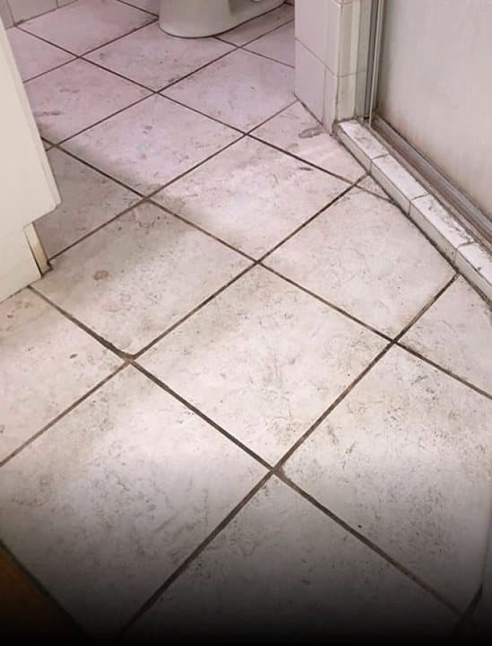 Grey bathroom floor tiles with dark dirty grout before cleaning