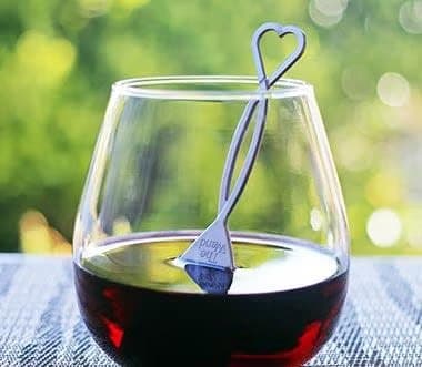 A PureWine wand with a heart-shaped top resting in a glass of red wine outdoors