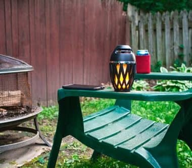 TikiTunes glowing on a green garden bench beside a fire pit and a drink