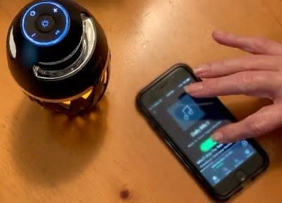 Hand selecting a TikiTunes speaker on a phone's Bluetooth screen beside the lit speaker