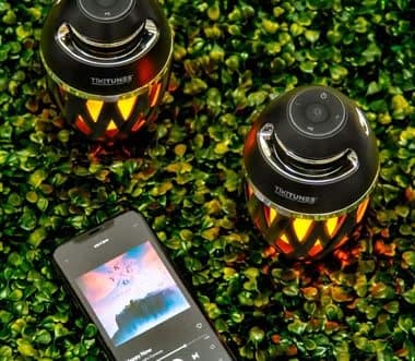 Two TikiTunes speakers on grass next to a phone playing music