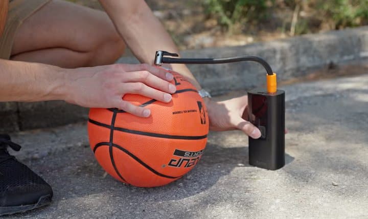 Person using a TireHero with a needle adapter to inflate a basketball
