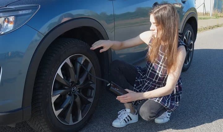 Woman crouching beside a car wheel using a TireHero inflator on the tire