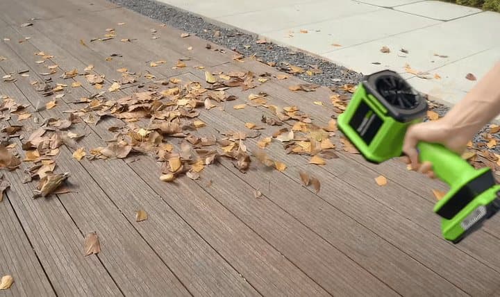 Hand using a green TornadoPro blower to clear dry leaves from a wooden deck