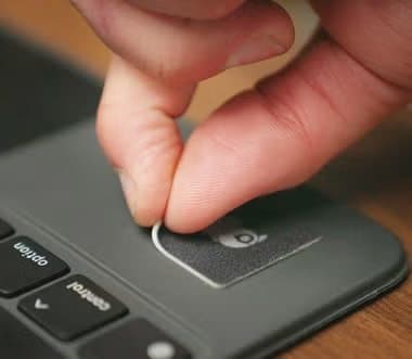 Fingers peeling a WaterBear patch off a laptop next to the keyboard