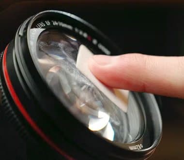 Finger wiping a large camera lens with a WaterBear patch