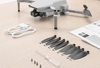 Grey folding drone on a wooden table with eight spare black propellers, screws, a screwdriver, a USB cable and a manual