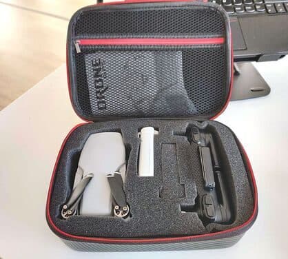 Open black and red zip case with foam cut-outs holding a folded grey drone, a battery and a controller