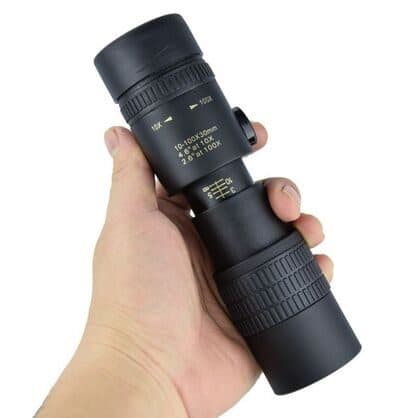 Hand holding the ZoomShot Pro monocular showing the markings 10-100x30mm, 4.6 degrees at 10x and 2.6 degrees at 100x, with a zoom lever